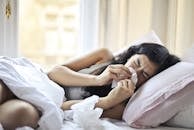 Een vrouw die in bed ligt te niezen, ter illustratie van de symptomen van hooikoorts